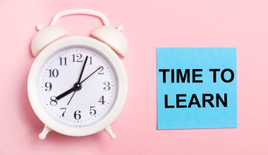Açık pembe bir arka planda, beyaz bir çalar saat ve üzerinde Time to EARN yazan mavi bir sayfa.
