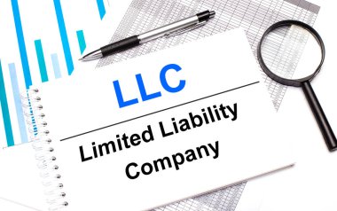 Masada raporlar, şemalar, bir kalem, bir büyüteç ve LLC Limited Limibility Company ile birlikte beyaz bir not defteri var. İş konsepti