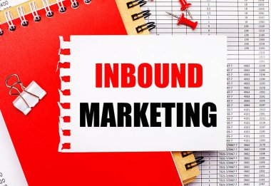 Raporların arka planında kırmızı ve kahverengi not defterleri, beyaz bir ataç, kırmızı düğmeler ve INBOUND MARKETING yazılı beyaz bir kağıt var. İş konsepti