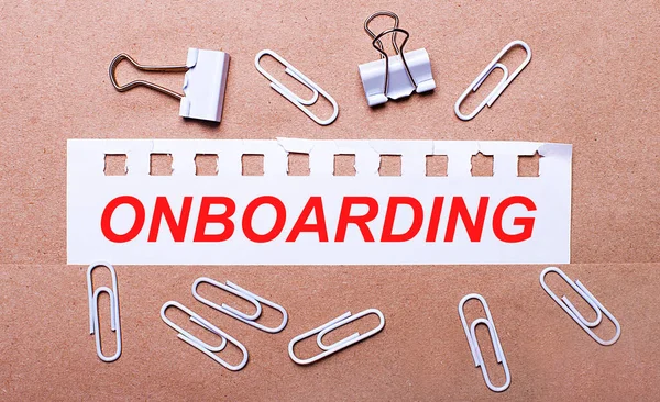 Kahverengi bir arka planda, beyaz ataçlar ve beyaz yırtık bir kağıt şeridi üzerinde ONBOARDING