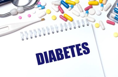 Açık bir arka planda, çok renkli haplar, bir steteskop, bir elektronik termometre ve DiABETES yazılı bir defter. Tıbbi konsept.