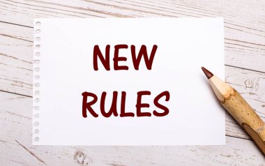 Hafif ahşap bir arka planda, renkli bir kalem ve üzerinde yeni kurallar yazan beyaz bir sayfa.