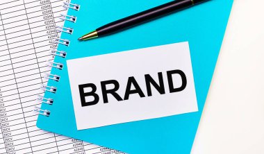 Ofis masasında raporlar, mavi bir not defteri, siyah bir kalem ve üzerinde Brand yazan beyaz bir kart var. Şık bir iş yeri. İş konsepti