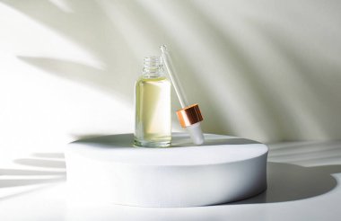 Yuvarlak bir podyumda açık yeşil bir arka planda sarı yağlı cam bir şişe var. Yanında pipet olan bir kep var. Gölgeler. Güzellik ve tıp kavramı