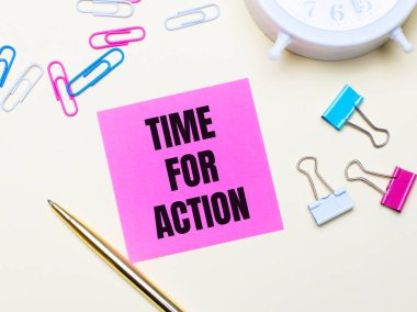 Hafif bir arka planda, beyaz bir çalar saat, pembe, mavi ve beyaz ataçlar, altın bir kalem ve üzerinde Time for Action yazan pembe bir çıkartma.