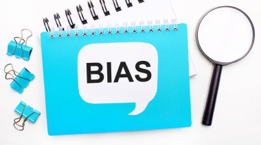 Mavi not defterli ofis masası, ataçlar, büyüteç ve BIAS yazılı beyaz kart. Üst manzara, düz yatış. Şık bir iş yeri