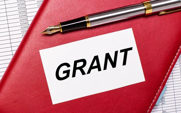 Masaüstünde raporlar, bordo bir defter, dolmakalem ve GRANT yazılı beyaz bir kart var. İş konsepti