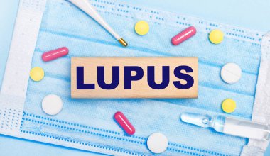 Açık mavi tek kullanımlık yüz maskesinde tabletler, bir termometre, bir ampul ve LUPUS yazılı ahşap bir blok vardır. Tıbbi konsept