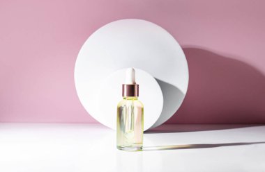 Açık pembe arka planda, bir cam yağ şişesi yuvarlak beyaz podyumların zemininde duruyor. Güzel gölgeler. Güzellik ve sağlık konsepti