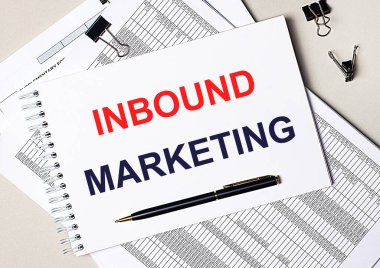 Masaüstünde belgeler, kalem, siyah ataçlar ve INBOUND MARKETING yazılı bir defter var. İş konsepti