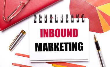 Masaüstünde INBOUND MARKETING, bir kalem, bordo ve kırmızı masalar ve altın çerçeveli gözlük yazılı beyaz bir defter var. İş konsepti.
