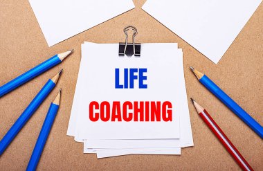 Açık kahverengi arka planda, mavi ve kırmızı kalemler ve üzerinde LIFE COACHING yazan beyaz kağıt