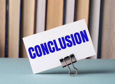 CONCLUSION metninin bulunduğu beyaz kart, kitapların arka planına karşı masada duran kağıtlar için bir şarjör üzerinde duruyor. Odaklanmayın