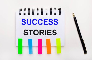 Hafif bir arkaplanda, bir kalem, içinde SUCCESS Hikayeleri ve parlak çıkartmalar olan bir defter..