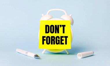 Açık mavi bir arkaplanda - beyaz bir kol ve üzerine parlak sarı bir çıkartma yapıştırılmış bir çalar saat metni unutmayın