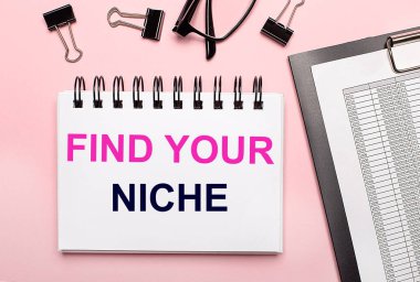 Pembe arka planda, raporlar, siyah ataçlar, gözlükler ve beyaz bir defter var.