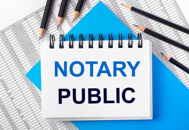 Üzerinde NOTARY PUBLIC yazan beyaz defter mavi arka planda siyah kalemlerin yanında ve raporlar. İş konsepti