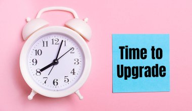 Açık pembe bir zemin üzerinde, beyaz bir çalar saat ve üzerinde Time to UPGRADE metni olan mavi bir sayfa.
