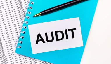 Ofis masasında raporlar, mavi bir not defteri, siyah bir kalem ve AUDIT yazılı beyaz bir kart var. Şık bir iş yeri. İş konsepti