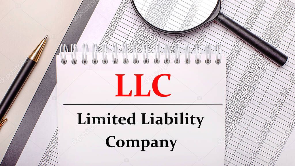 Desktop magnifier, reports, pen and notebook with text LLC Limited Liability Company. Business concept
