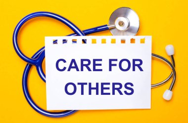 Parlak sarı bir zemin üzerinde mavi bir steteskop ve üzerinde diğerleri için özen gösteren bir kağıt var. Tıbbi konsept