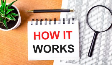 Tahta bir masanın üzerinde raporlar, saksı bitkisi, bir büyüteç, siyah bir kalem ve nasıl çalıştığını anlatan bir defter var. İş konsepti