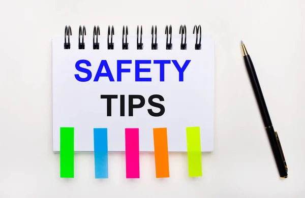 On a light background, a pen, a notebook with the text SAFETY TIPS and bright stickers.