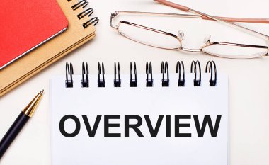 Hafif arkaplanda altın çerçeveli gözlükler, bir kalem, kahverengi ve kırmızı not defterleri ve üzerinde 