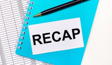 Ofis masasında raporlar, mavi bir not defteri, siyah bir kalem ve üzerinde RECAP yazan beyaz bir kart var. Şık bir iş yeri. İş konsepti
