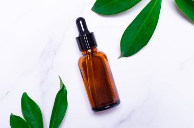 Açık mermer arka planda, bir bitkinin yeşil yaprakları ve yağ için kahverengi bir cam şişe. Konteynır. Metin eklenecek yer. Tıp ve güzellik konsepti. Şablon