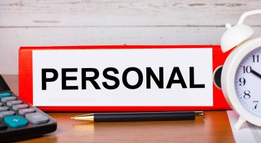 Yazılı kağıtlar için kırmızı klasör PERSONAL, beyaz alarm saati, hesap makinesi ve kalem masaüstünde. İş konsepti