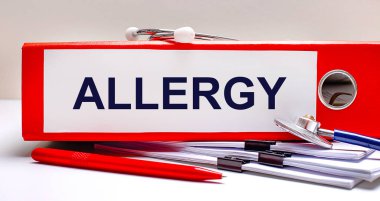 Masaüstünde steteskop, dokümanlar, bir kalem ve içinde ALLERGY metni olan kırmızı bir dosya klasörü var. Tıbbi konsept