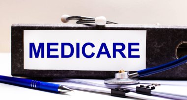 Masaüstünde stetoskop, mavi bir kalem ve MEDICARE metninin olduğu gri bir dosya klasörü vardır. Tıbbi konsept
