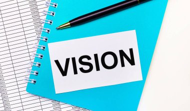 Ofis masasında raporlar, mavi bir not defteri, siyah bir kalem ve üzerinde VISION yazan beyaz bir kart var. Şık bir iş yeri. İş konsepti