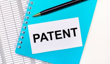 Ofis masasında raporlar var. Mavi bir not defteri, siyah bir kalem ve içinde PATENT yazan beyaz bir kart. Şık bir iş yeri. İş konsepti
