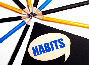 Çok renkli kalemlerin yanında siyah arkaplan üzerinde HABITS yazılı tahta kart.