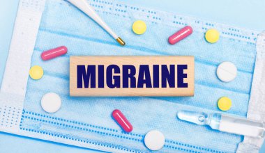 Açık mavi tek kullanımlık yüz maskesinde tabletler, bir termometre, bir ampul ve MIGRAINE yazılı ahşap bir blok bulunur. Tıbbi danışma