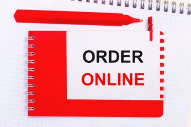 Beyaz bir not defterinde, kırmızı bir kalem, kırmızı bir not defteri ve üzerinde ORDER ONLINE yazan beyaz bir sayfa.
