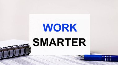 Açık gri bir arkaplanda, bir defter, mavi bir kalem ve üzerinde SMARTER yazan bir kağıt. İş konsepti