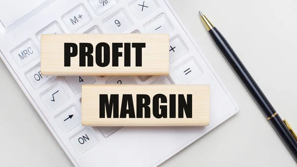 Beyaz bir hesap makinesinin arka planında ProFIT MARGIN ile ahşap bloklar. Yakınlarda siyah bir kol var. İş konsepti