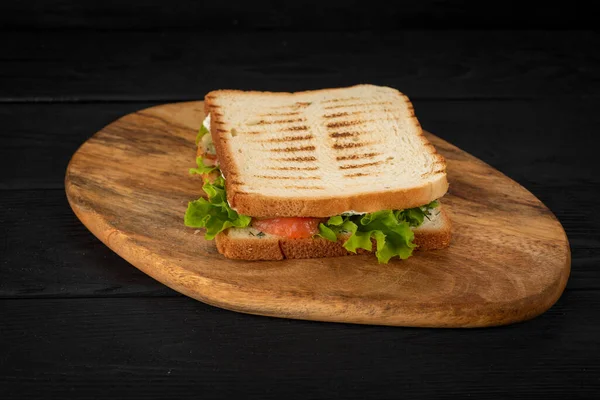 Yeşillikli sandviç, tahtadan yapılmış balık ve siyah arka plan.