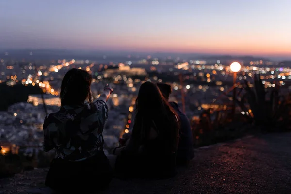Arkadaşlar gün batımının son saatlerinin tadını çıkarıyorlar. Şehrin ışıklarını tepeden izliyorlar.