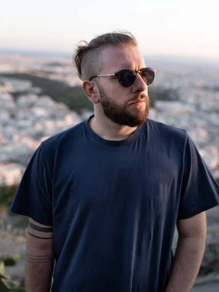 Gün batımında güneş gözlüklü, sakallı ve at kuyruklu genç adam portresi