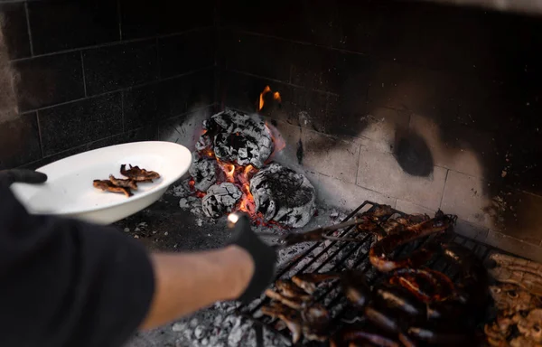 Неузнаваемый человек забирает мясо с дровяного барбекю с углем на заднем плане. Закрыть. — стоковое фото