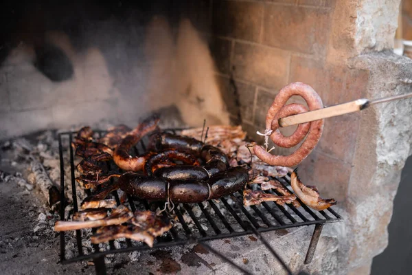 Неузнаваемый человек бросает колбасу на дровяное барбекю с различными видами мяса. Закрыть. — стоковое фото
