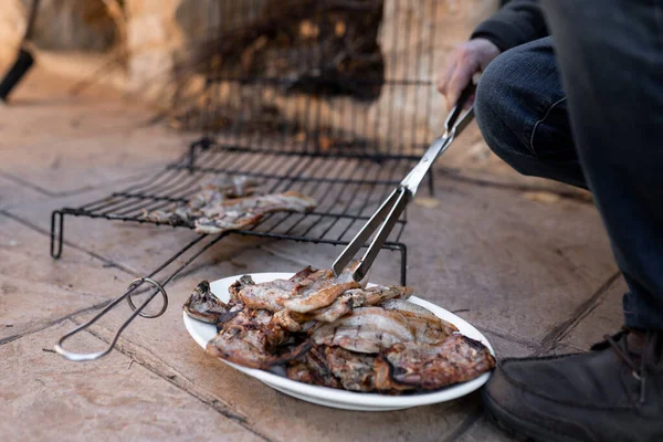 Неузнаваемый взрослый мужчина использует щипцы, чтобы положить гриль приготовленную пищу на тарелку после барбекю — стоковое фото