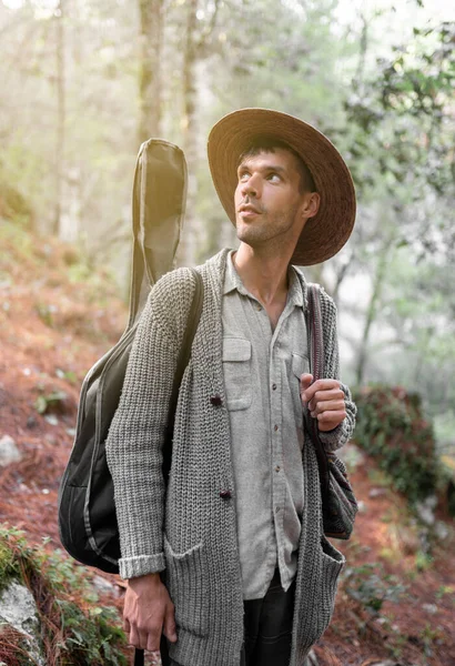 Genç erkek müzisyen ormanda gitarını ve çantasını taşırken ilham arıyor. Doğada eğlenme kavramı
