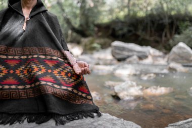 Hand of a young man meditating by the river sitting on a rock. Close up. Concept of spiritualism in the nature.