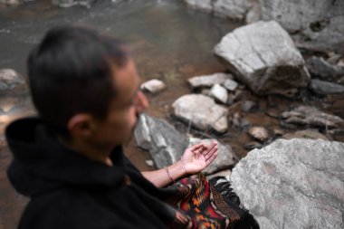 Young man meditating by the river wearing a poncho. Concept of spiritualism in the nature
