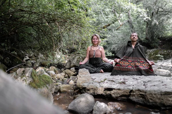 A young couple is meditating in a river sitting on a rock. Concept of spiritualism in the nature.